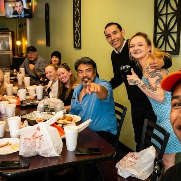 A large group of diverse people smiling and posing for a photo at a restaurant table.