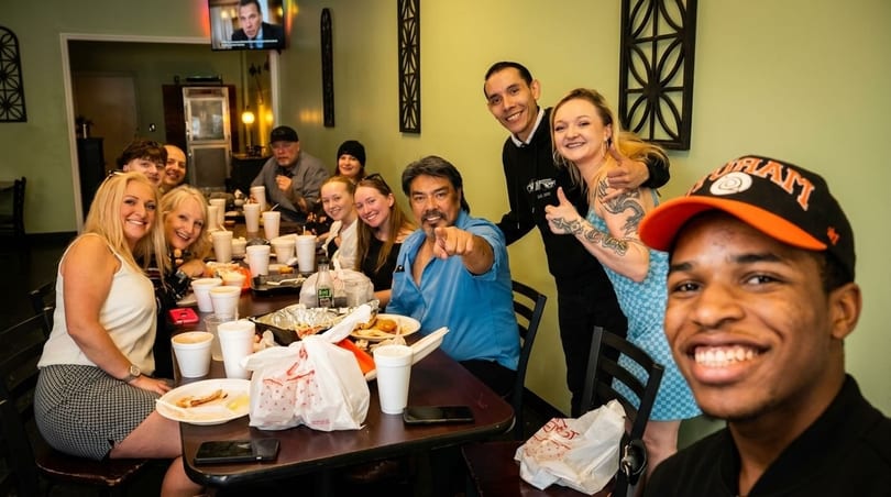 A large group of diverse people smiling and posing for a photo at a restaurant table.