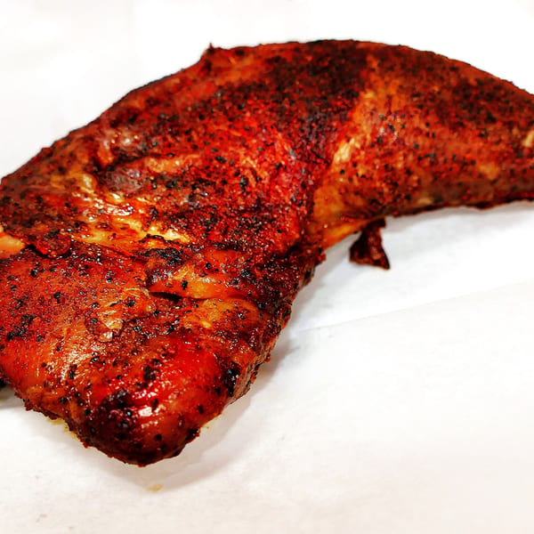 A close-up of a perfectly cooked, seasoned chicken leg quarter on a white surface.