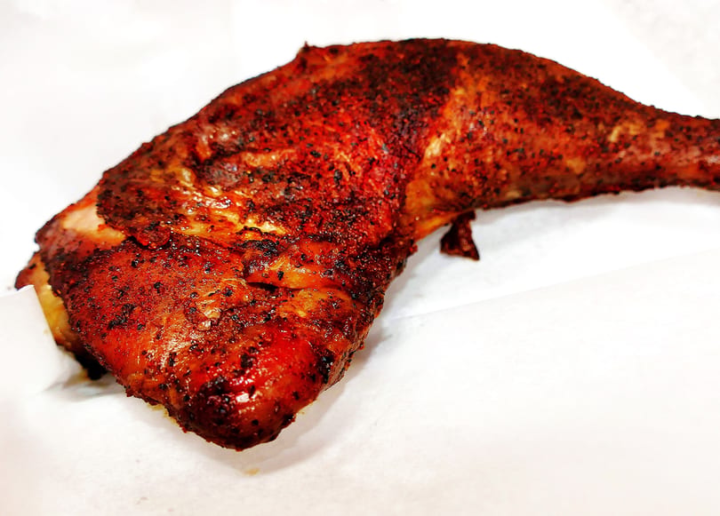 A close-up of a perfectly cooked, seasoned chicken leg quarter on a white surface.