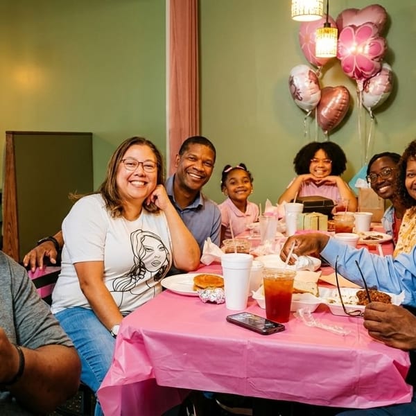 A large family smiles at the camera while sitting around a table with food and drinks.
