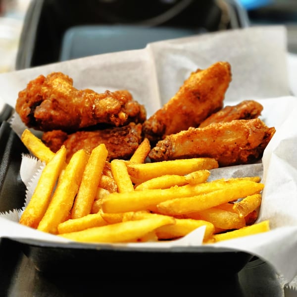 Crispy fried chicken wings and golden french fries served in a black basket lined with white paper.