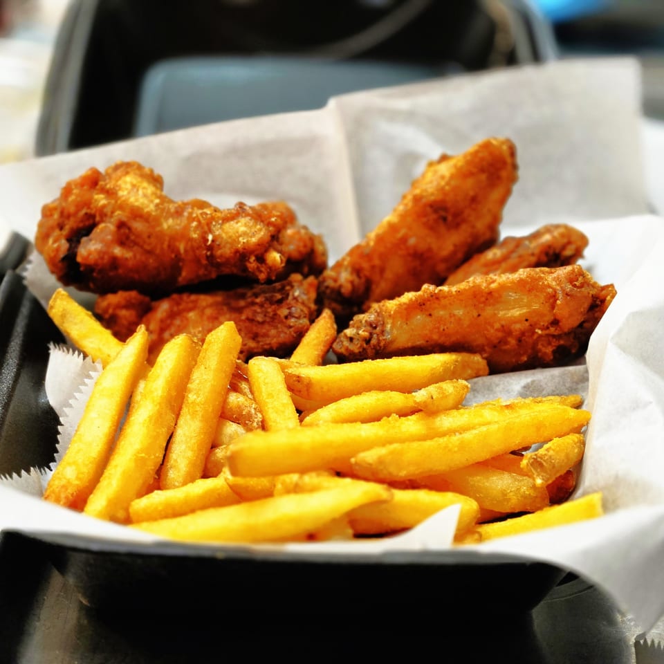 Crispy fried chicken wings and golden french fries served in a black basket lined with white paper.