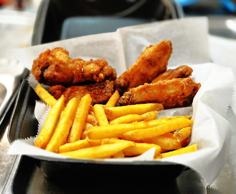 Crispy fried chicken wings and golden french fries served in a black basket lined with white paper.
