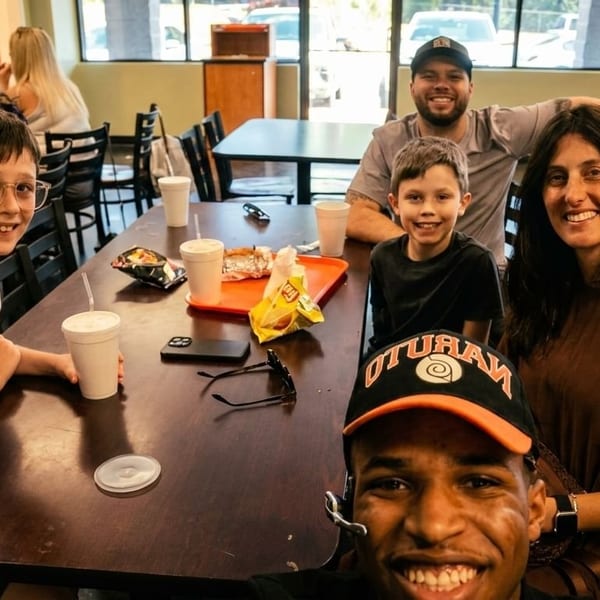 A family and friends smiling at a table in a casual restaurant, with food and drinks.