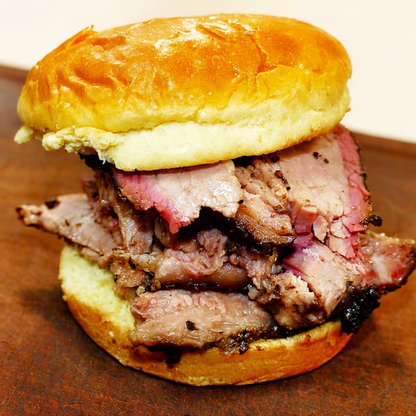A close-up of a brisket sandwich on a brioche bun, showcasing the juicy, smoked meat.
