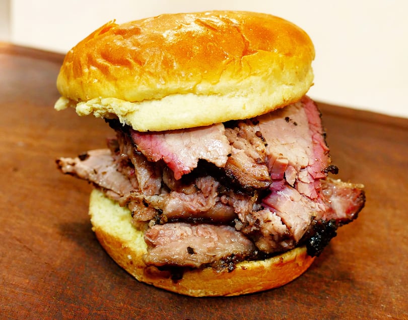 A close-up of a brisket sandwich on a brioche bun, showcasing the juicy, smoked meat.