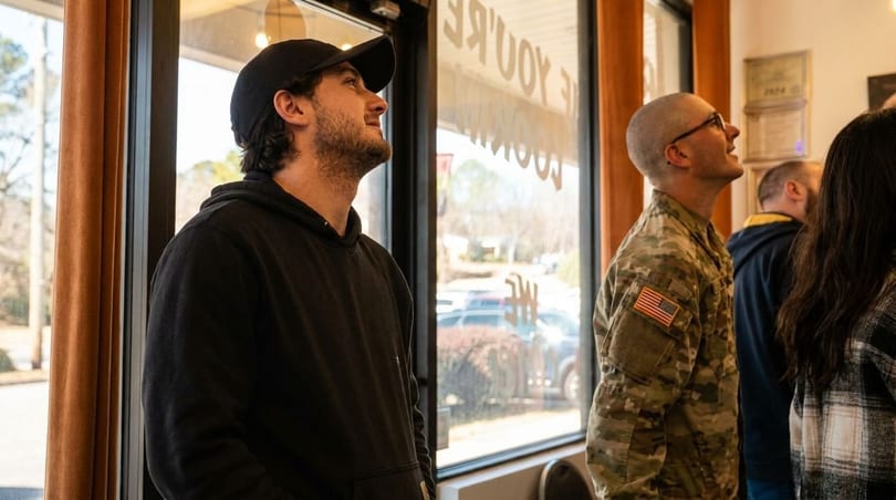 Customers, including a man in military uniform, look up inside a restaurant with large windows.