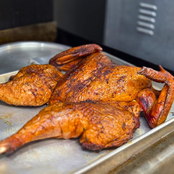 A whole roasted chicken, golden brown and crispy, rests on a metal baking sheet.