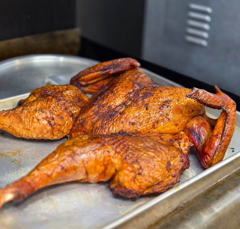 A whole roasted chicken, golden brown and crispy, rests on a metal baking sheet.