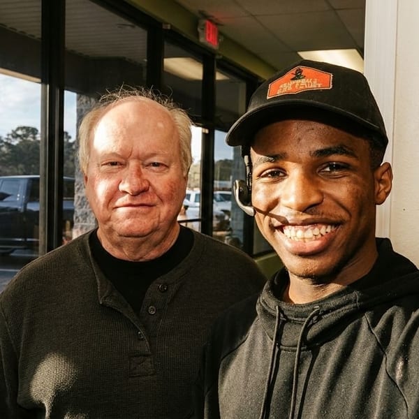 Two men, one older and one younger, smiling at the camera indoors.