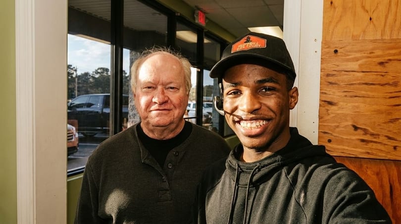 Two men, one older and one younger, smiling at the camera indoors.