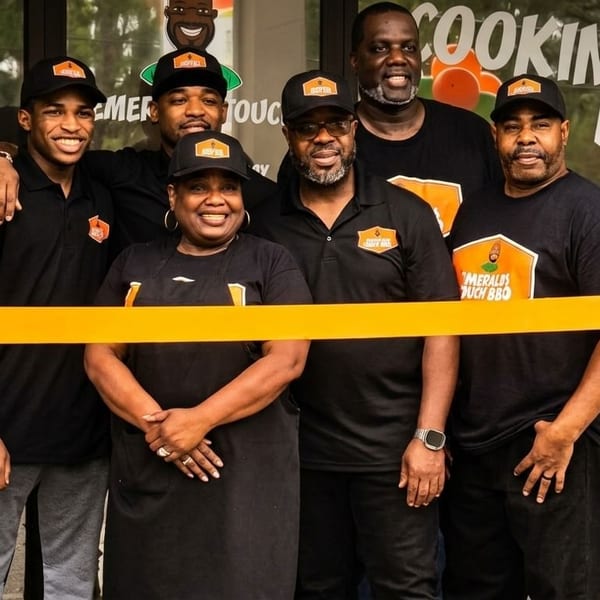 Six smiling people in black shirts and hats stand behind a yellow ribbon in front of a restaurant.