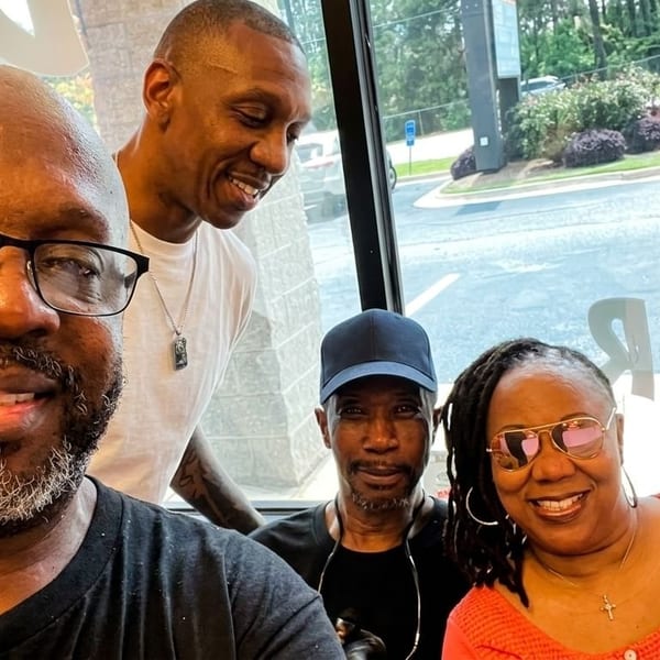 Four smiling people, two men and two women, pose for a selfie inside a restaurant with window views.