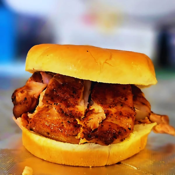 Close-up of a grilled chicken sandwich on a bun, with crispy skin and juicy meat.