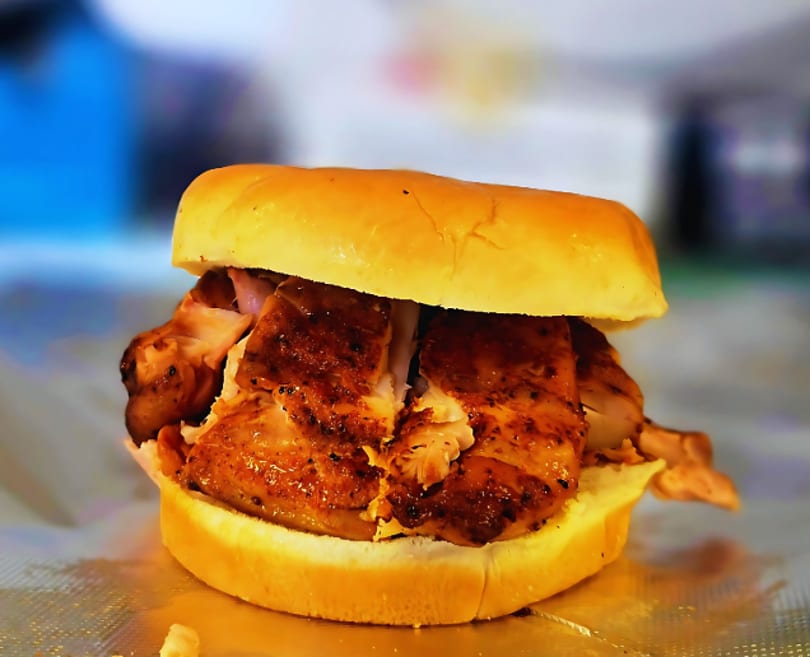 Close-up of a grilled chicken sandwich on a bun, with crispy skin and juicy meat.