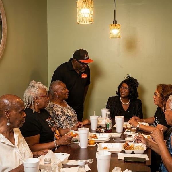 A group of people, mostly women, dining at a restaurant table with a server standing nearby.