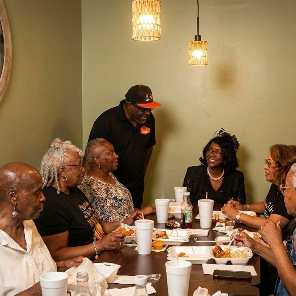 A group of people, mostly women, dining at a restaurant table with a server standing nearby.
