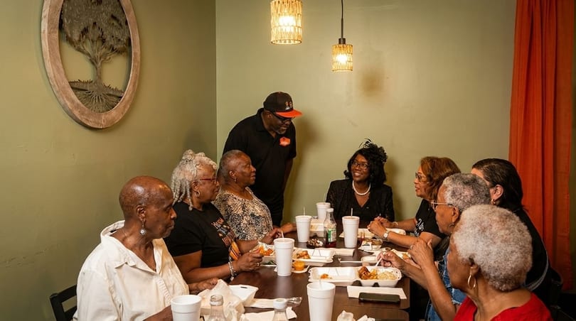 A group of people, mostly women, dining at a restaurant table with a server standing nearby.