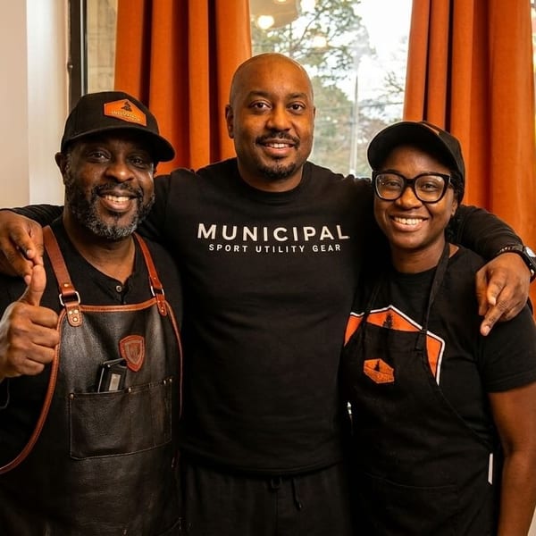 Three smiling restaurant staff members, two men and one woman, pose together in front of a window.